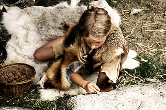 Young girl in primitive fur clothing sitting on animal hide outdoors