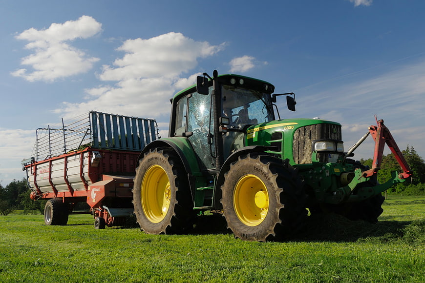 Green John Deere Tractor Pulling Hay Trailer in Pasture