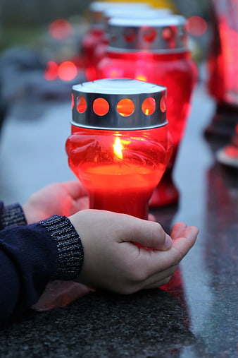 Child's hands holding a red memorial candle at a cemetery grave