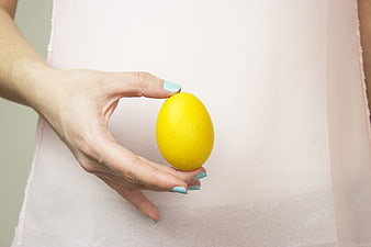 Woman's hand holding a yellow Easter egg against a white dress