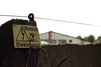 Weathered wooden fence post with German high voltage warning sign