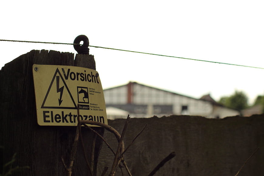 Weathered wooden fence post with German high voltage warning sign