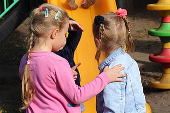Two young girls talking and gesturing at a colorful playground
