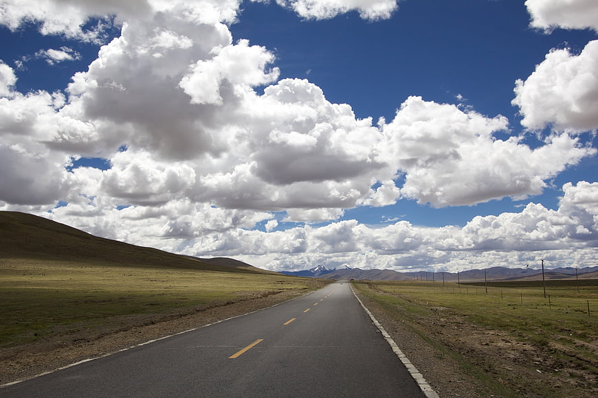 Straight Highway Through Green Hills Under Cloudy Blue Sky
