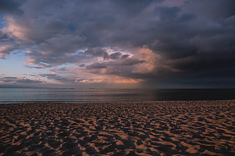Dramatic sunset over sandy beach with textured ripples and moody clouds