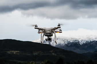 White drone flying over mountains with camera