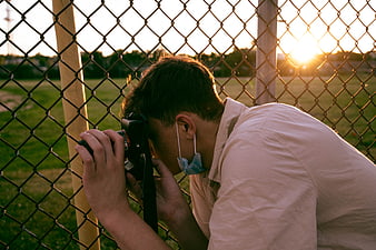 Man with Camera Peering Through Chain Link Fence at Sunset