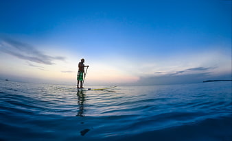 Man paddleboarding on calm ocean at sunset