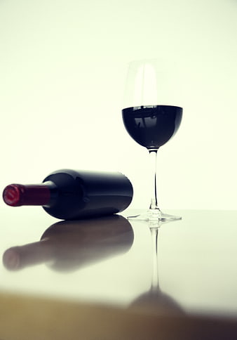 Red wine bottle and glass on reflective white table