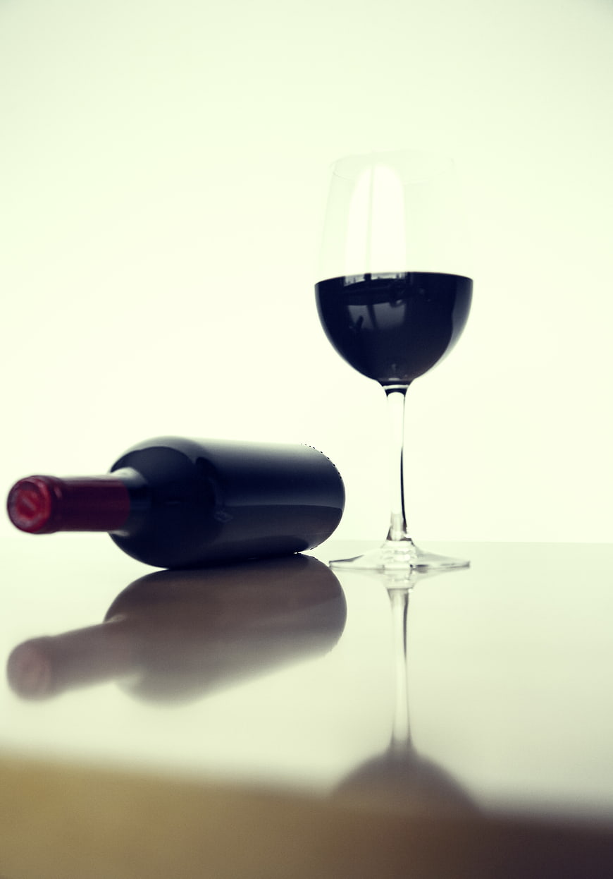 Red wine bottle and glass on reflective white table