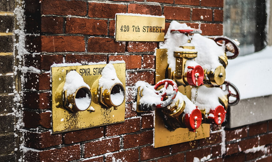 Snow-covered fire hydrant on brick wall in winter