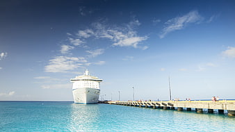 White cruise ship docked at a long pier in turquoise sea