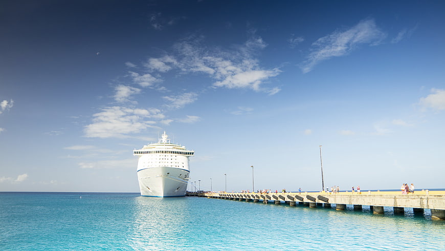White cruise ship docked at a long pier in turquoise sea