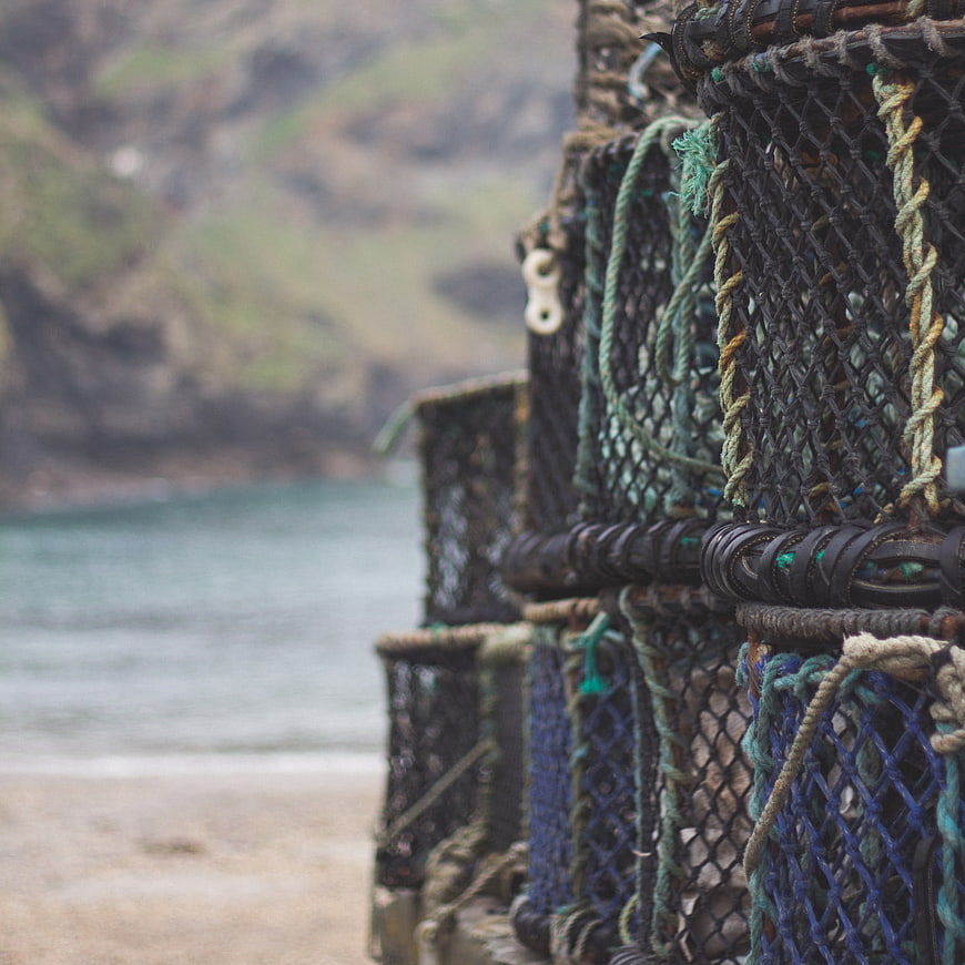 Stacked lobster pots on a coastal beach with blurred ocean background