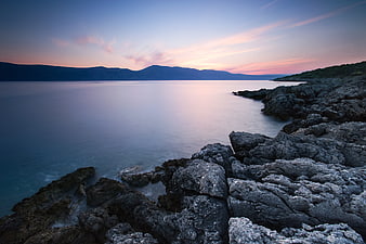 Serene Sunset Over Rocky Coastline with Smooth Ocean Water