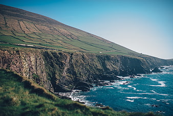 Dramatic coastal cliffs with terraced hills and turquoise ocean waves