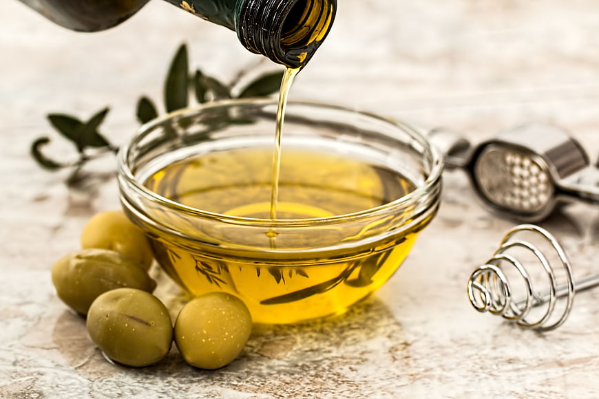 Pouring Olive Oil into Glass Bowl with Fresh Olives