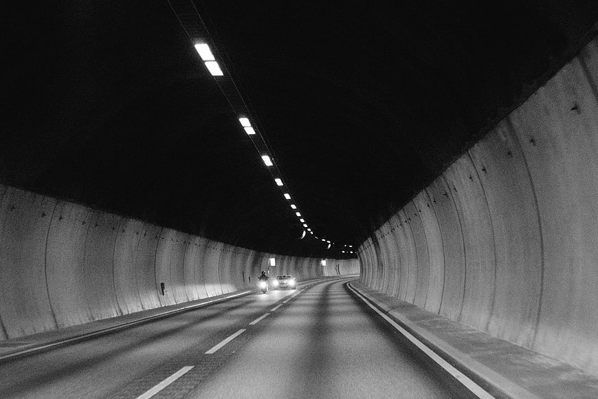 Black and white photo of a motorcycle and car driving through a tunnel