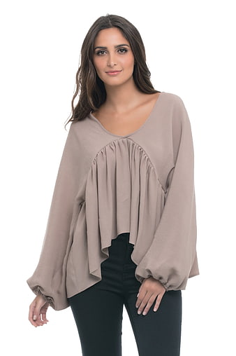 Female model wearing beige ruffled blouse and black jeans on white background