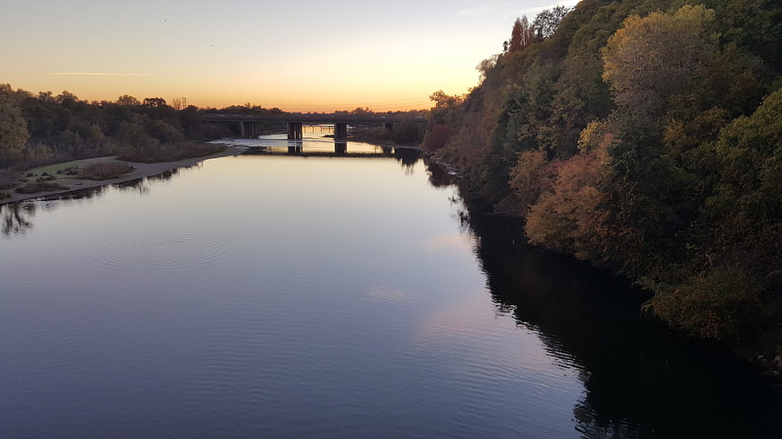 Serene River Sunset with Autumn Trees and Bridge