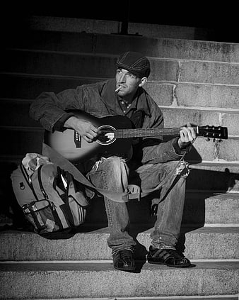 Homeless street musician playing guitar on concrete steps