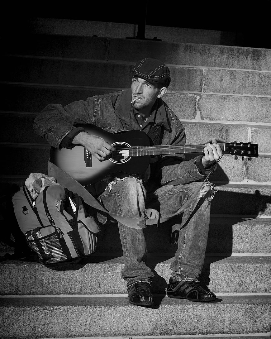 Homeless street musician playing guitar on concrete steps