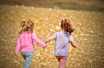 Two young girls holding hands walking away on a rocky path