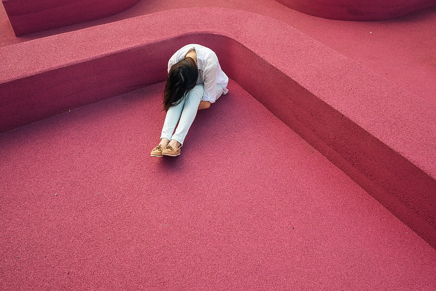Woman sitting alone on pink curved steps looking down