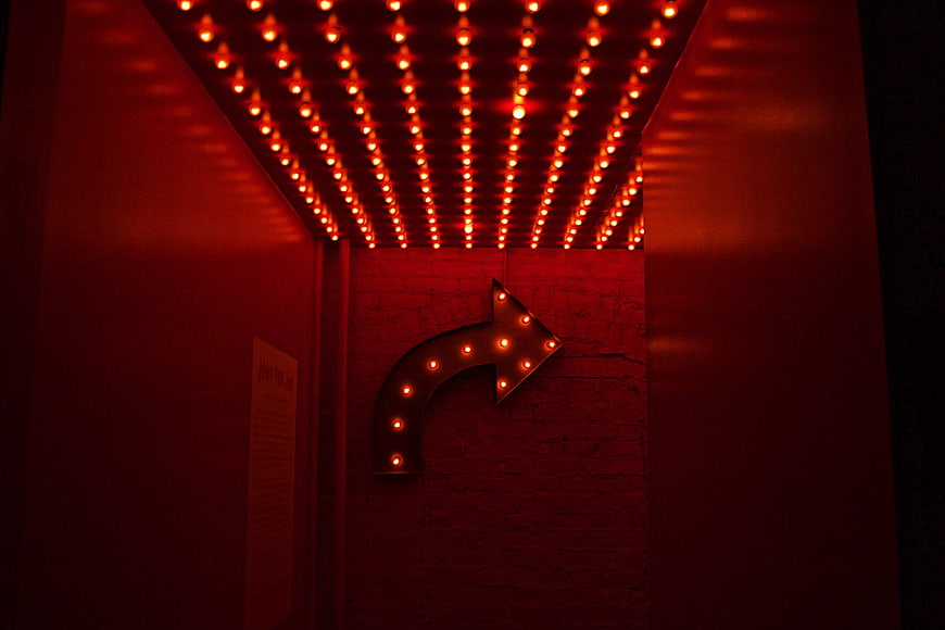 Red Marquee Arrow Sign in Dark Corridor with Ceiling Lights