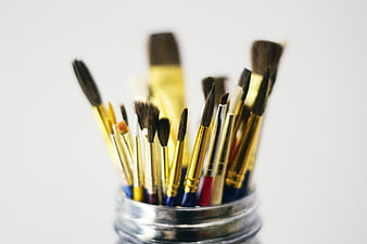 Collection of paintbrushes in a glass jar on white background