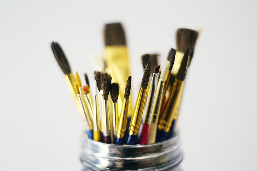 Collection of paintbrushes in a glass jar on white background