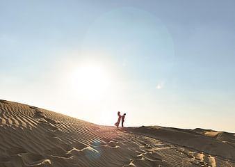Silhouette of couple embracing on sand dune at sunset