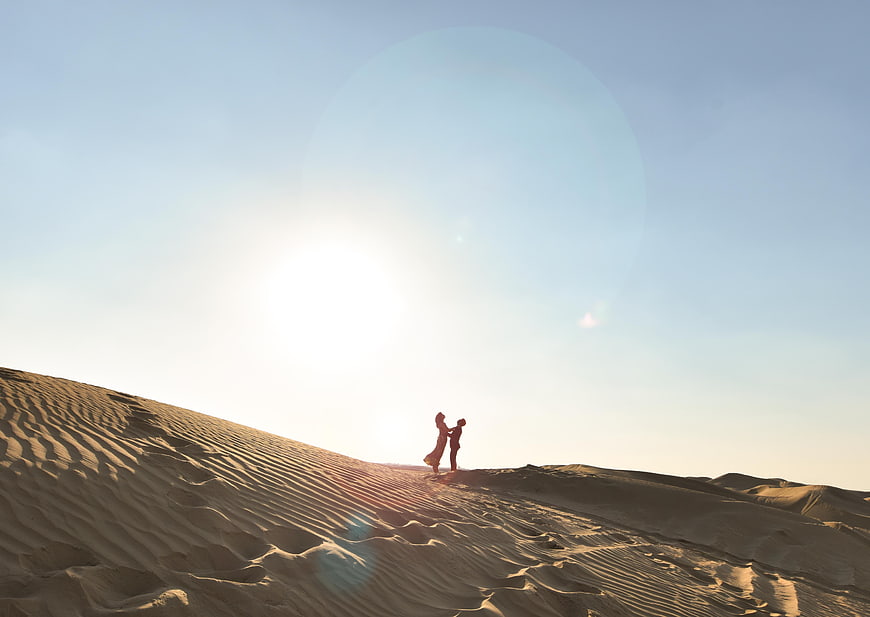 Silhouette of couple embracing on sand dune at sunset