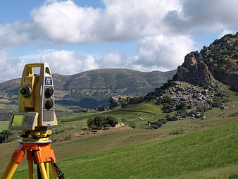 Yellow Total Station Surveying Equipment on Green Mountain Landscape