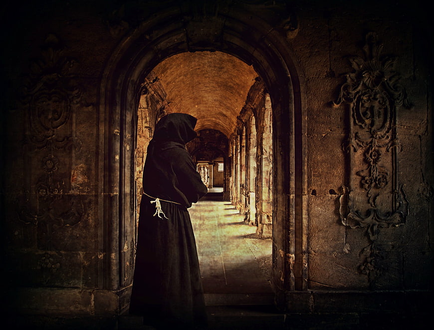 Hooded Monk Standing in Ancient Stone Cloister Corridor