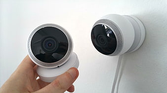 Hand holding white security camera next to wall mounted unit