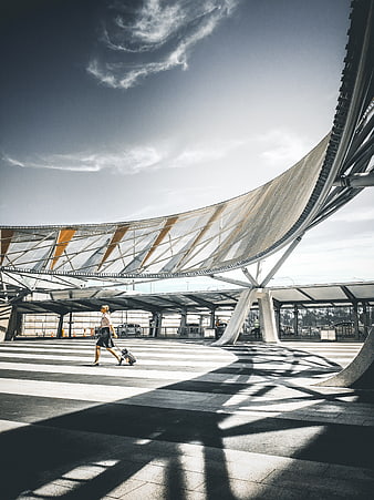 Woman with suitcase walking under modern airport terminal architecture