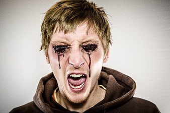 Young man with bloody eyes and screaming expression in brown hoodie