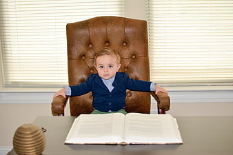 Toddler boy in navy blazer sitting in large leather office chair
