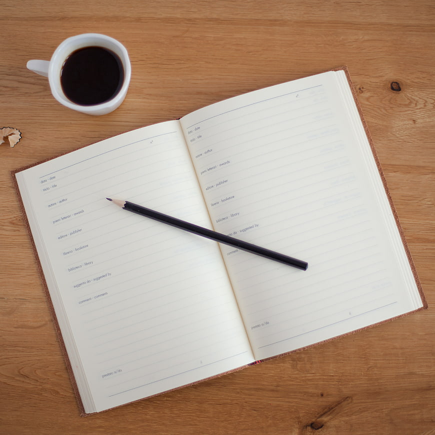 Open notebook with pencil and coffee on wooden desk