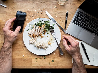 Overhead view of man eating chicken and rice at desk with laptop