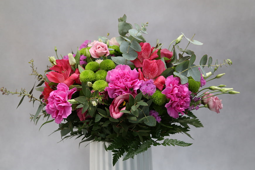 Colorful floral arrangement in a white vase against a gray background