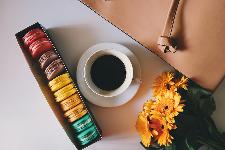 Flat lay of colorful macarons, coffee, flowers, and handbag