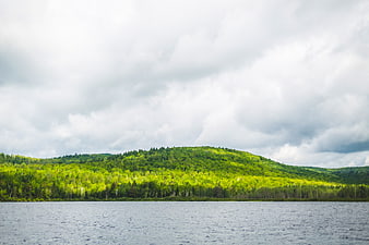 Lush Green Forested Hills Over Lake Under Cloudy Sky