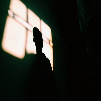 Silhouette of a man standing in a dark room with window light