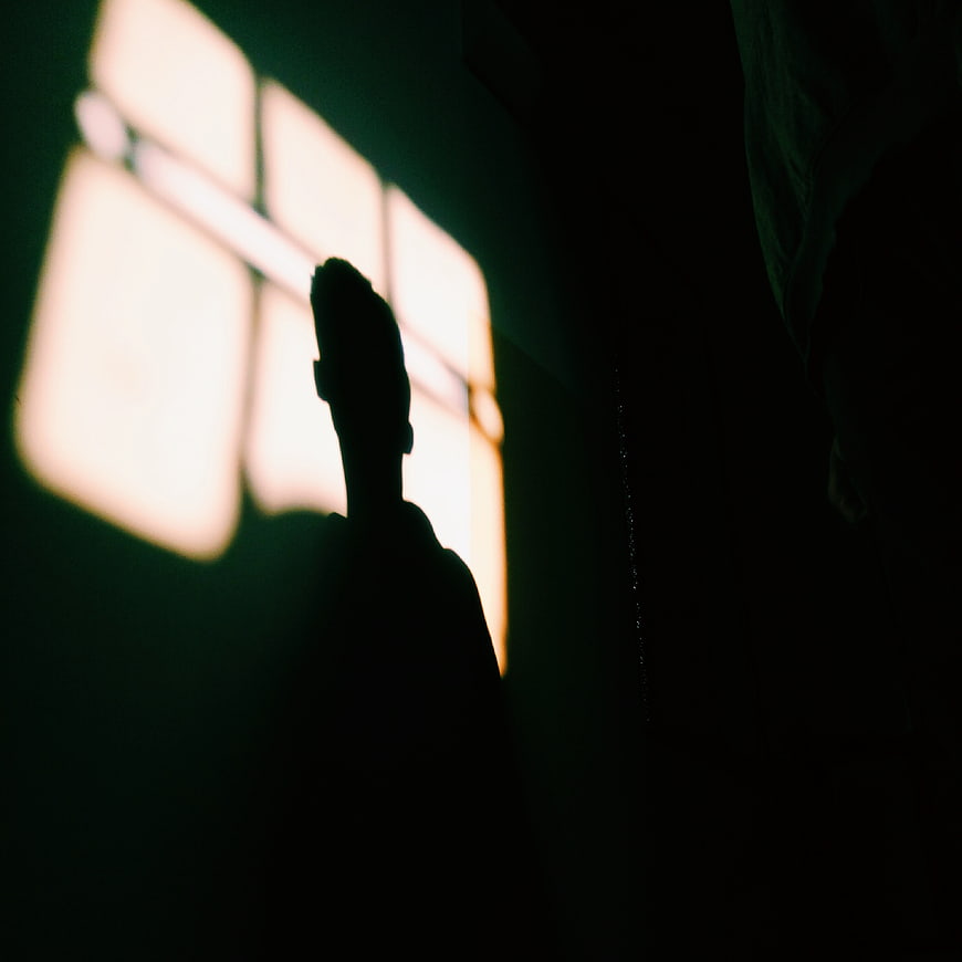 Silhouette of a man standing in a dark room with window light