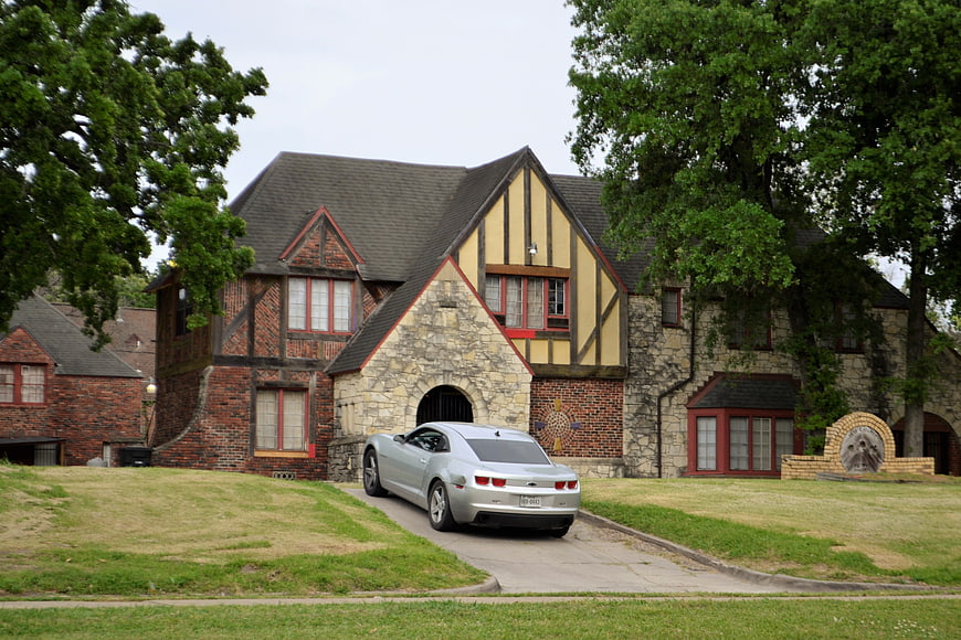 Silver Ford Mustang Parked In Front Of Large Tudor-Style Brick House