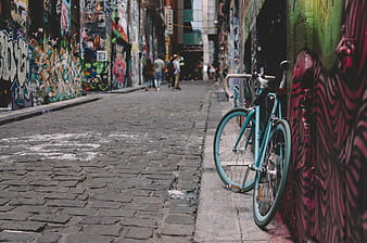Teal Bicycle Leaning Against Graffiti Wall in Cobblestone Alley