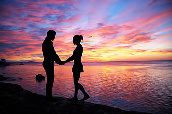 Silhouette of a couple holding hands at a colorful sunset beach
