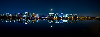 Panoramic night skyline of Seoul with moon and river reflections
